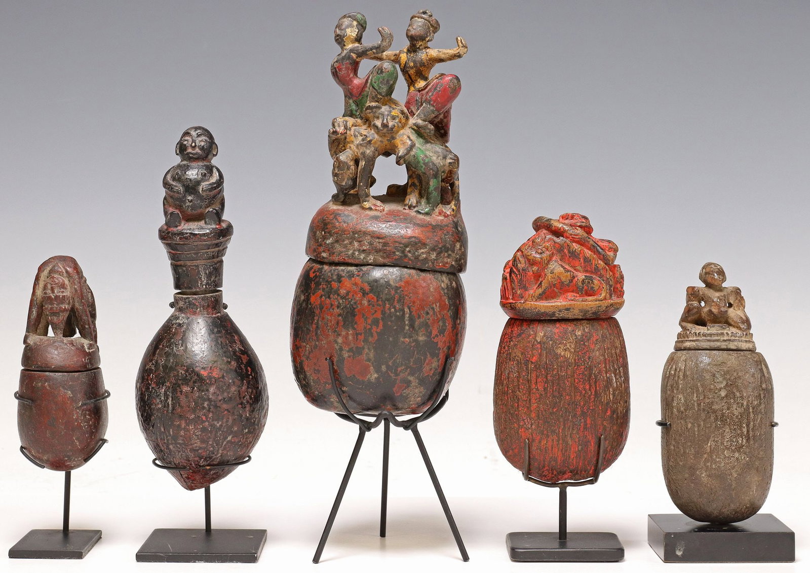 (5) CARVED & PAINTED SEED POD BOXES ON DISPLAY STANDS: (lot of 5) Carved and polychrome painted seed pod boxes, possibly Southeast Asia, varied designs, each having lid modeled as a figure or group of figures, most in dynamic pose, accompanied by met