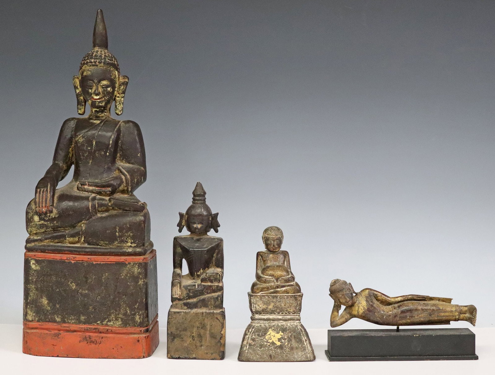 (4) SOUTHEAST ASIAN CARVED WOOD BUDDHA FIGURES: (lot of 4) Southeast Asian carved wood Buddha figures, each retaining remnants of gilt paint, including: (2) seated Buddhas, in the Bhumisparsha (earth touching) Mudra, (1) recumbent Buddha,