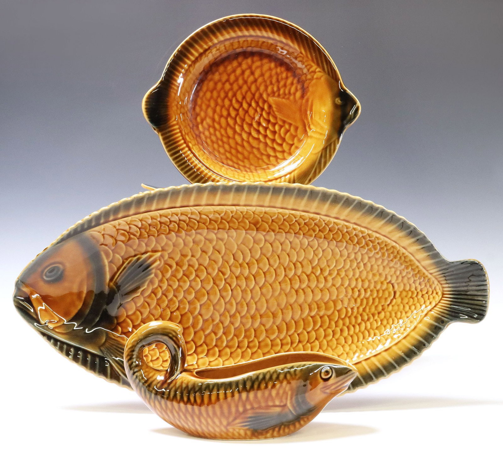(14) FRENCH SARREGUEMINES FAIENCE FISH SERVICE: (lot of 14) French faience fish service, Sarreguemines, 20th c., in and brown and green glaze, each modeled as a fish with textured scales, maker's mark underfoot, including: (12) plates, app