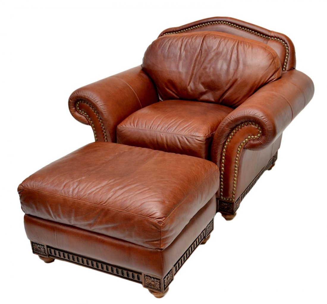 JOHN WILLIAMS INTERIOR LEATHER CHAIR & OTTOMAN: (lot of 2) John Williams Interior leather chair and matching ottoman, the oversized chair having rolled arms, brass nail head trim on the whole, carved floral heads on each corner of the carved frame
