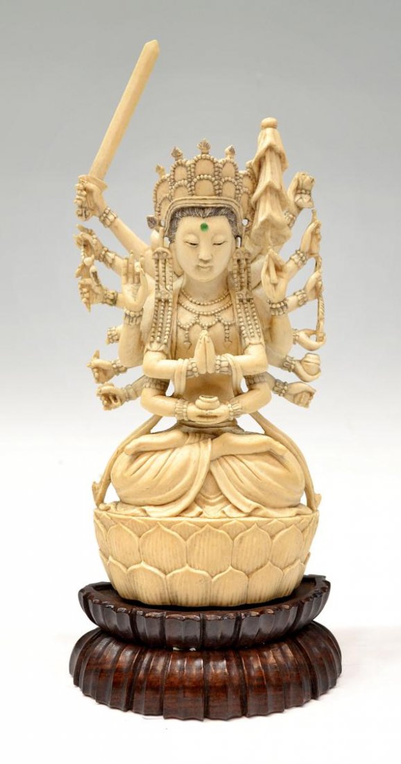CHINESE CARVED IVORY MULTI ARM DEITY ON BASE: **International shipping is not available on this lot** A Chinese carved ivory deity seated in the lotus position upon a raised lotus pedestal, adorned in elaborate jewelry and headdress with green bi