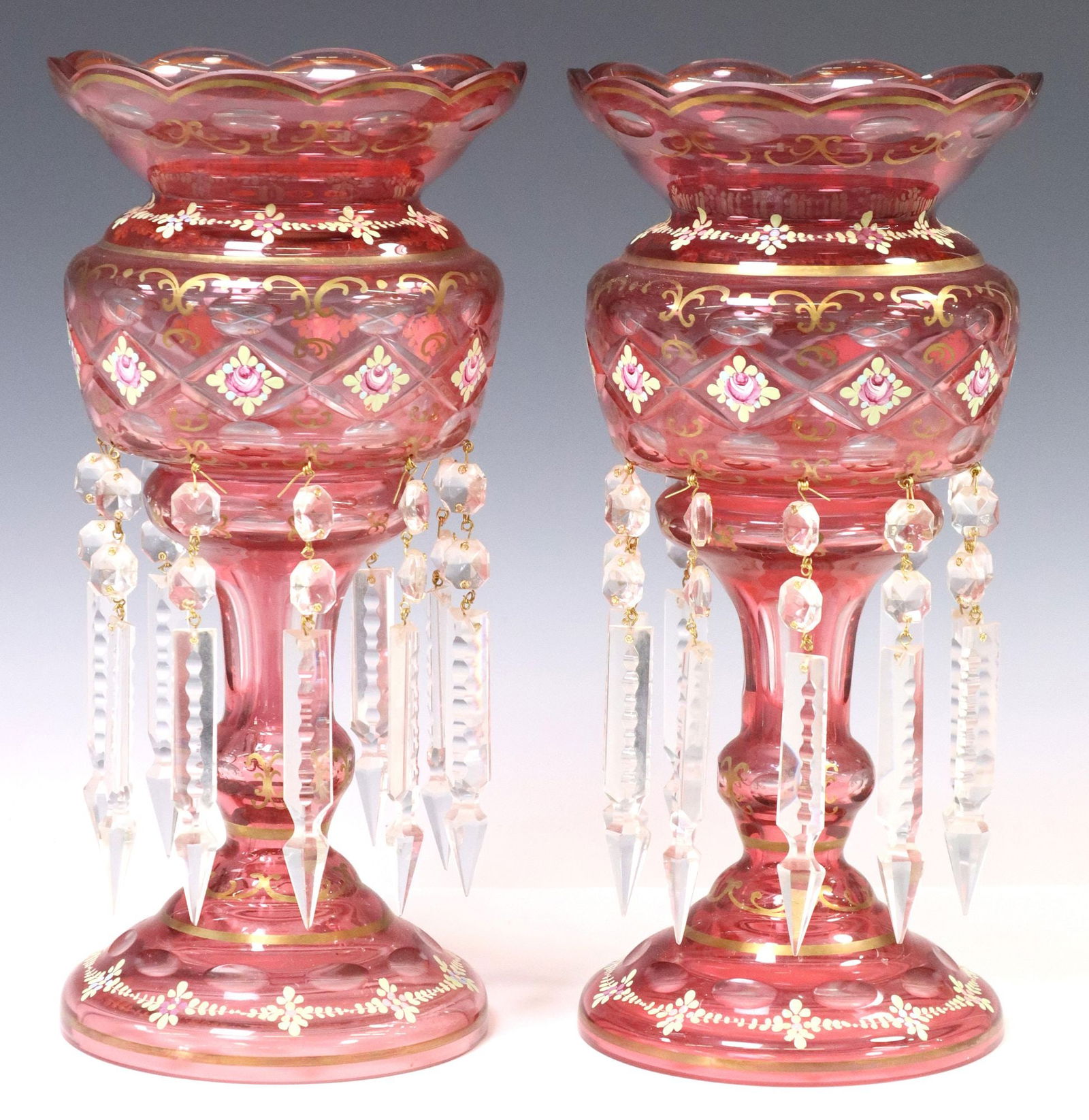(2) ENAMELED & PARCEL GILT COLORED GLASS MANTEL LUSTERS: (pair) Parcel gilt glass mantle lusters, 20th c., having scalloped rim, over, hand-painted foliates and gilt scrolling trim, faceted standard, hung with crystal prisms, rising on cut round base, each