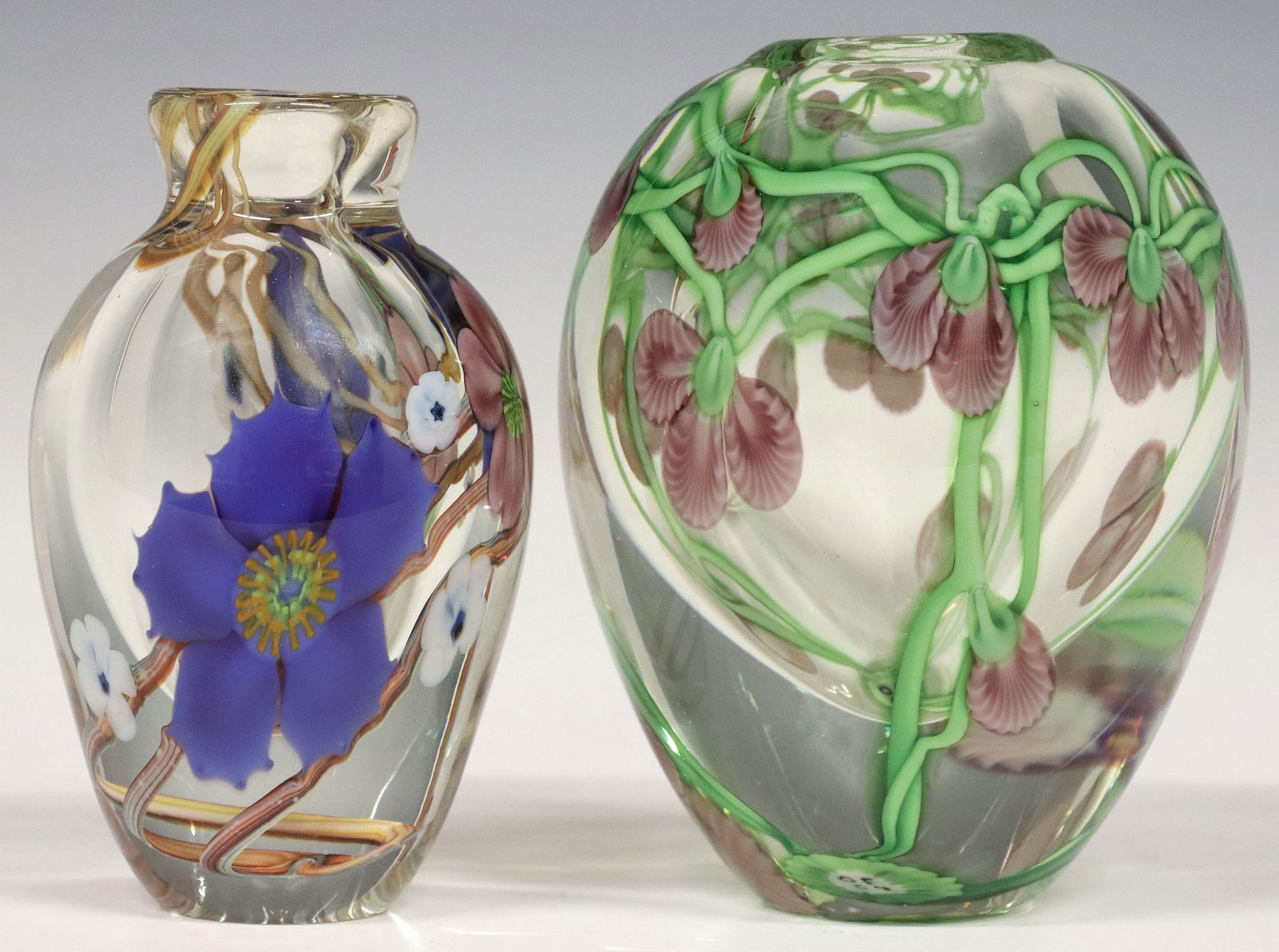 (2) GREG HELD & BRUCE SILLARS ORIENT & FLUME GLASS PAPERWEIGHT VASES: (lot of 2) Studio art glass paperweight vases, Orient and Flume, each having double-walled colorless case, with lampwork flowers on foliate vines, including: (1) signed Held (Greg Held, American, 1951