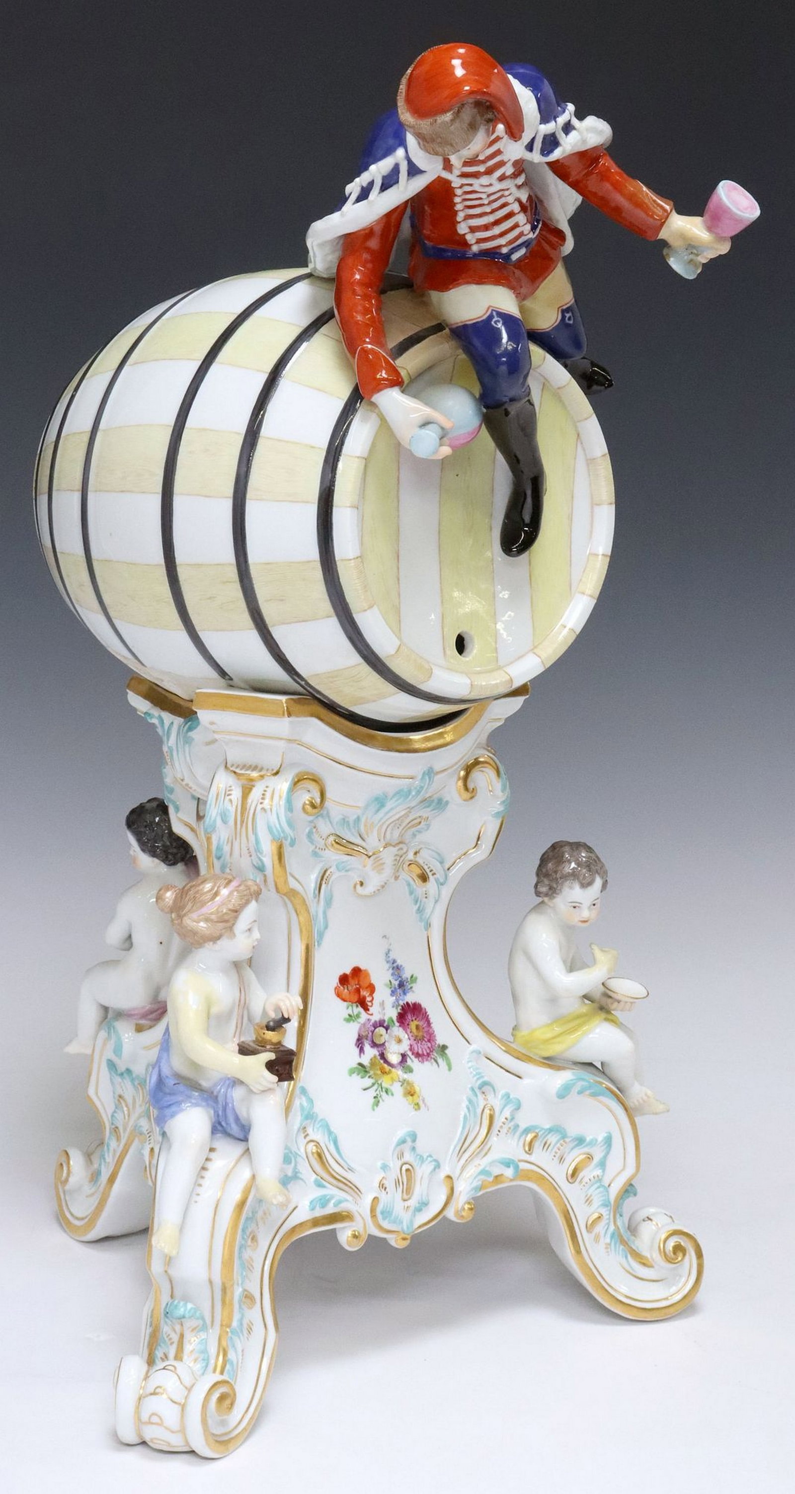 MEISSEN PORCELAIN SOLDIER SPIRIT BARREL ON STAND: Meissen parcel gilt porcelain figural spirit barrel on stand, depicting drunken male figure in military uniform holding wine glass and bottle, on striped barrel with painted wood grain, rest