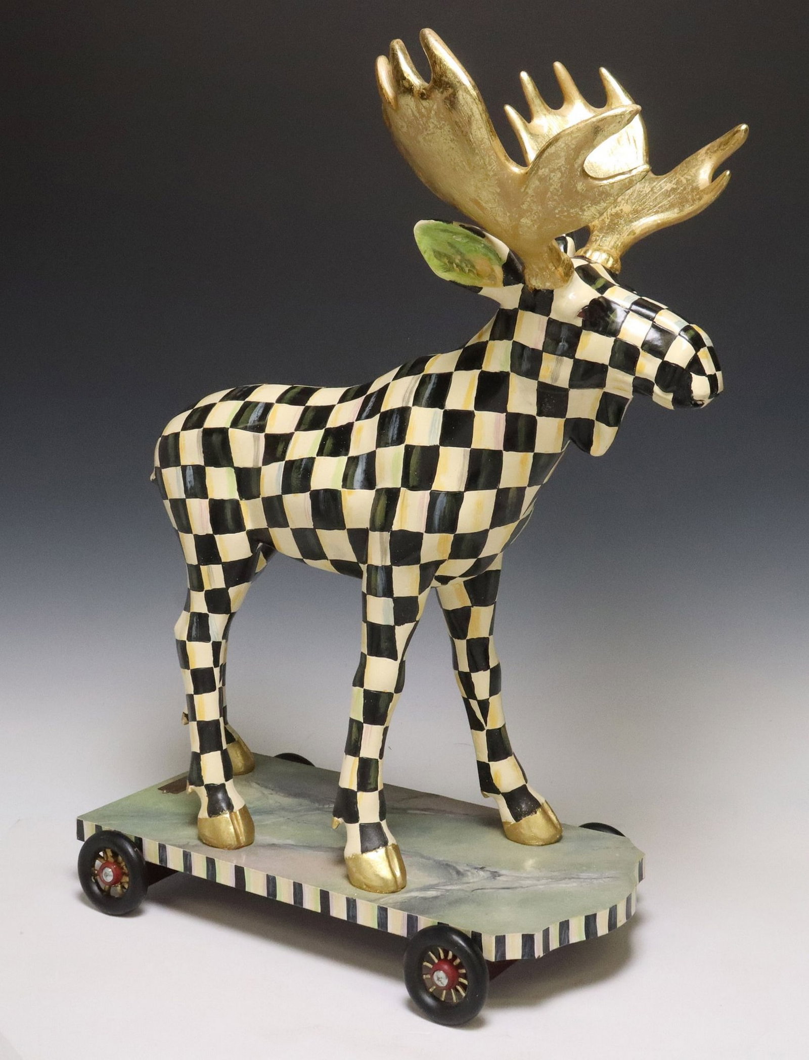 MACKENIZE-CHILDS 'COURTLY CHECK' RESIN CAST MOOSE ON PARADE: Mackenzie-Childs cast resin "Courtly Check Moose on Parade," having gilt-painted antlers and hooves, rising on marbleized base, ending on four integral wheels, maker's mark on base 