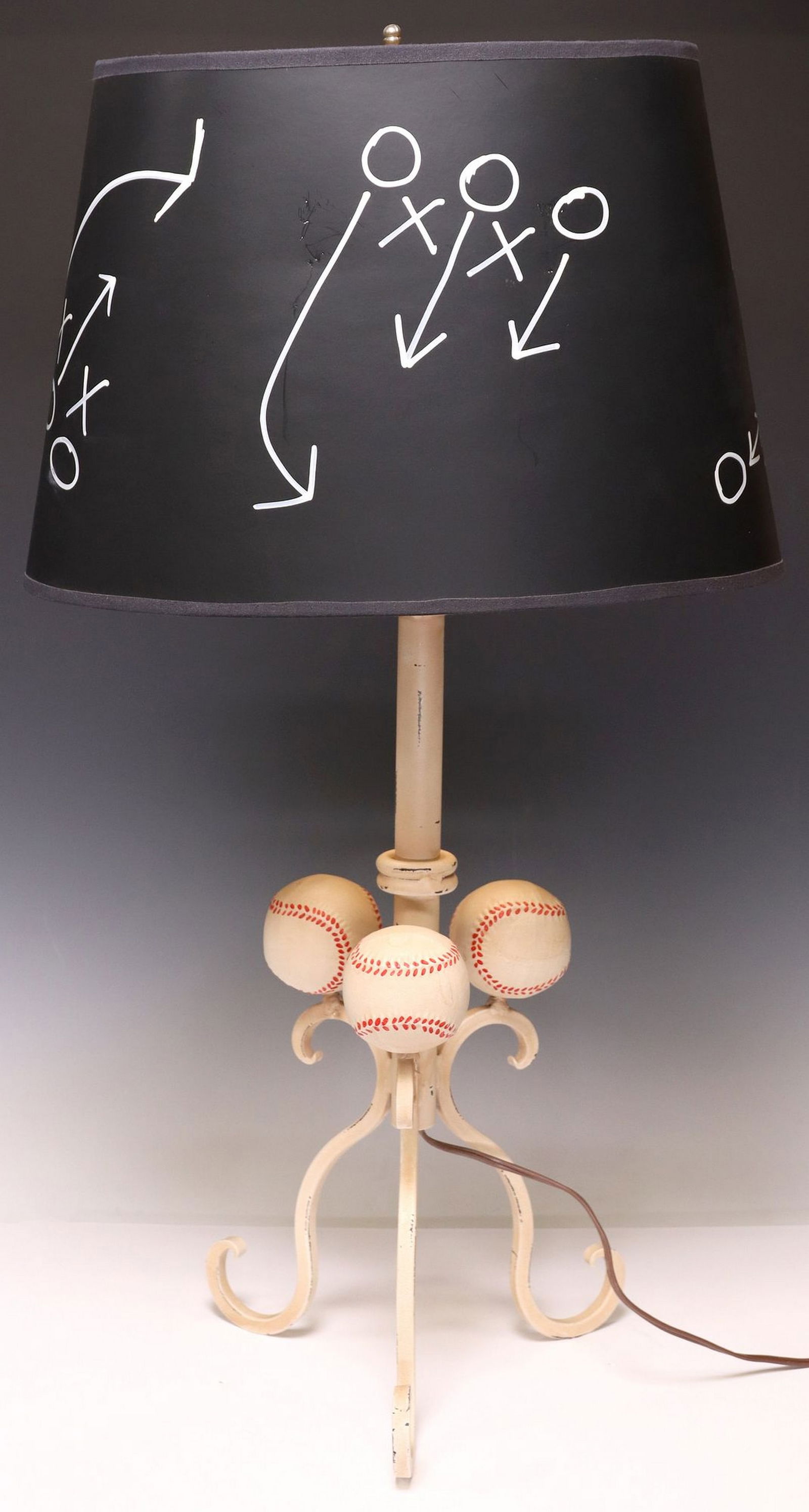 RUSTIC PAINT-DECORATED IRON 'BASEBALL' TABLE LAMP: Rustic paint-decorated iron table lamp, 20th c., matte black shade with painted playbook routes, enclosing single light, rising on cylindrical standard, issuing tripodal scroll legs, each topped