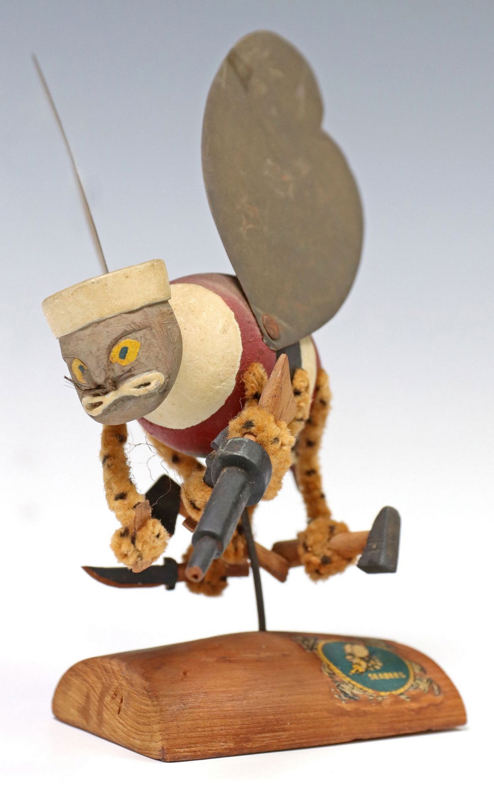 US NAVY SEABEE MODEL: U.S. Navy Seabee model, hand made with a mustached winged bee wearing a sailor hat and holding a machine gun, hammer, knife, and hatchet, the body and arms are multicolored, black metal wings, mounted