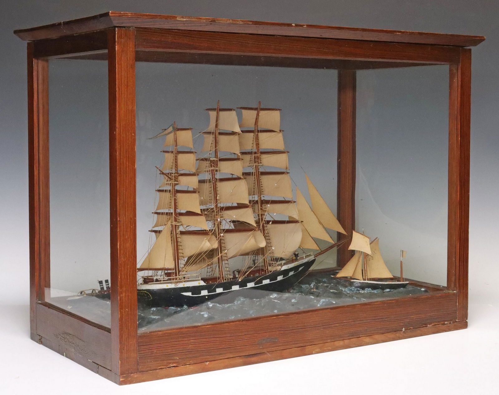 FRENCH BARQUE SAILING SHIP MODEL IN GLASS DISPLAY CASE: French sailing ship model, 20th c., glazed wood display case housing wood and ceramic barque ship, with string rigging and paper sails, rising on painted ocean waves beside two smaller vessels, signed