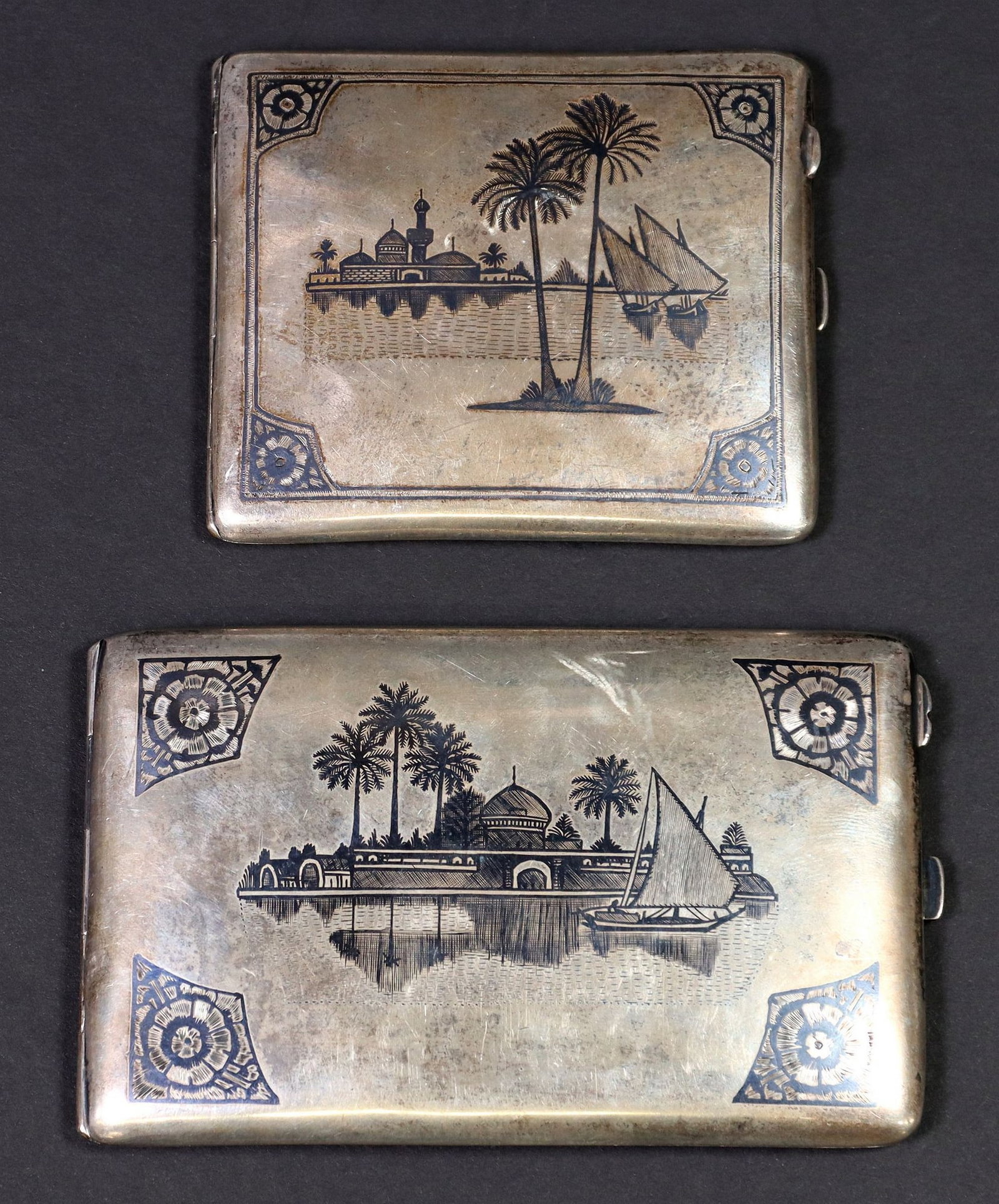 (2) IRAQI SILVER & NIELLO CIGARETTE CASES: (lot of 2) Iraqi silver (content unknown) and Niello cigarette cases, decorated with landscape scenes, including: (1) depicting a Mosque, the obverse with two camels and palm trees, interior engr