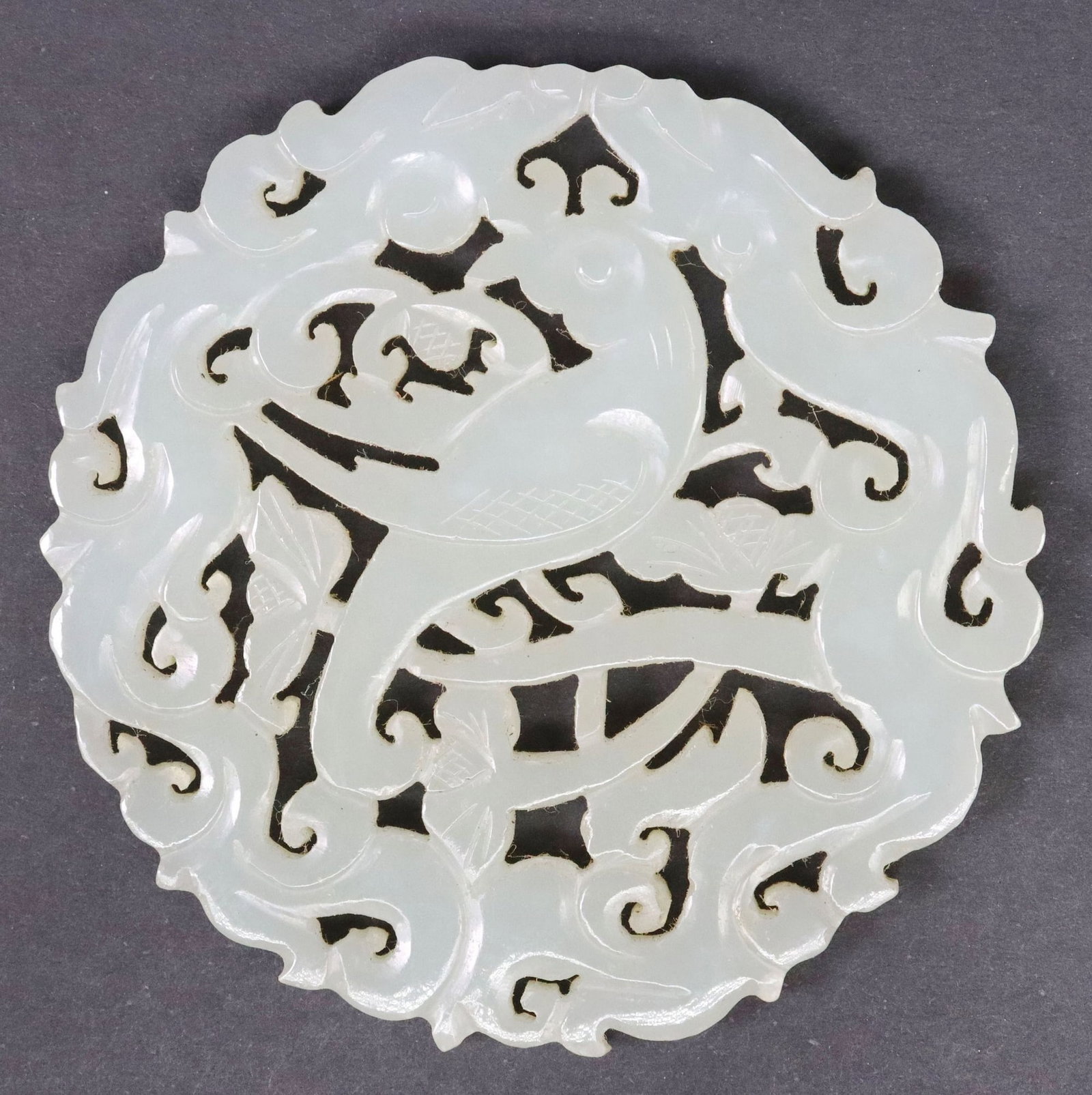 CHINESE CARVED GREEN HARDSTONE PENDANT PLAQUE WITH DRAGONS & BIRD: Chinese carved green hardstone pendant plaque, depicting central bird below two opposing dragons, among scrolled branches with foliate motifs, approx 2.25"diam, 26.4 grams