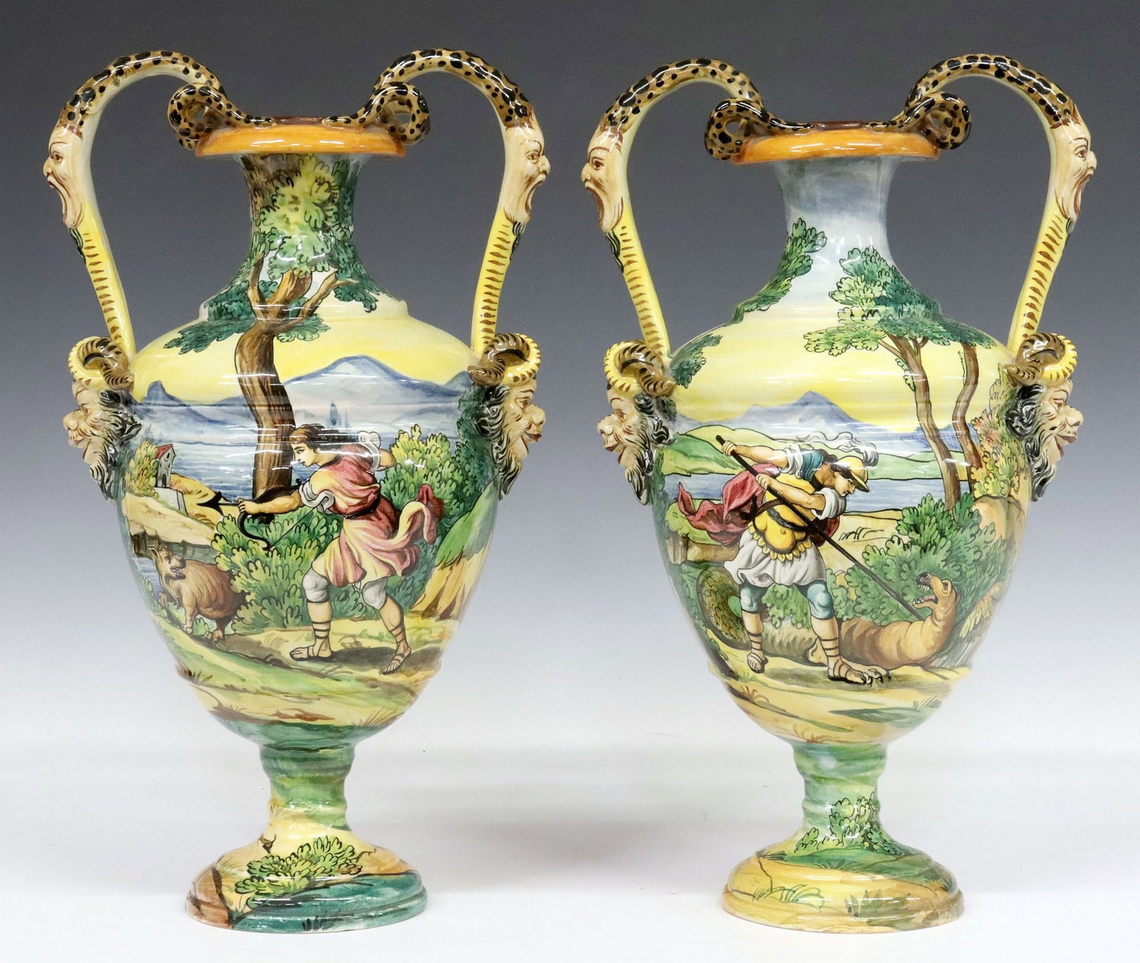 (2) ITALIAN HAND-PAINTED MAJOLICA POTTERY AMPHORA URNS: (lot of 2) Italian glazed majolica pottery amphorae, 20th c., each having dual scrolled handles with figural mask ends, with hand-painted scenes depicting allegorical figures battling mythical beasts,
