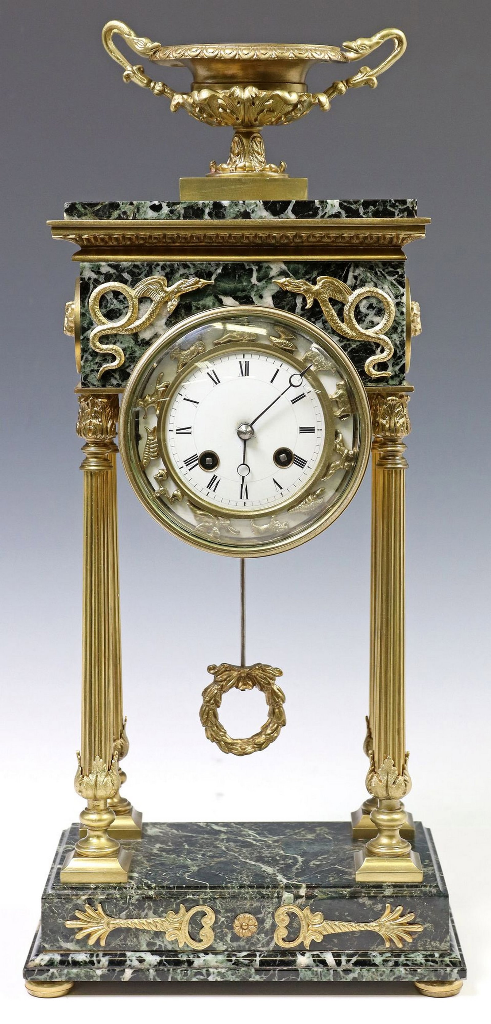 FRENCH EMPIRE STYLE GILT-METAL & MARBLE PORTICO CLOCK: French Empire style mantel clock, 20th c., urn-form finial, frieze with applied mounts of opposing winged serpents, white enamel dial with Roman numeral hours, surrounded by the twelve symbols of the 