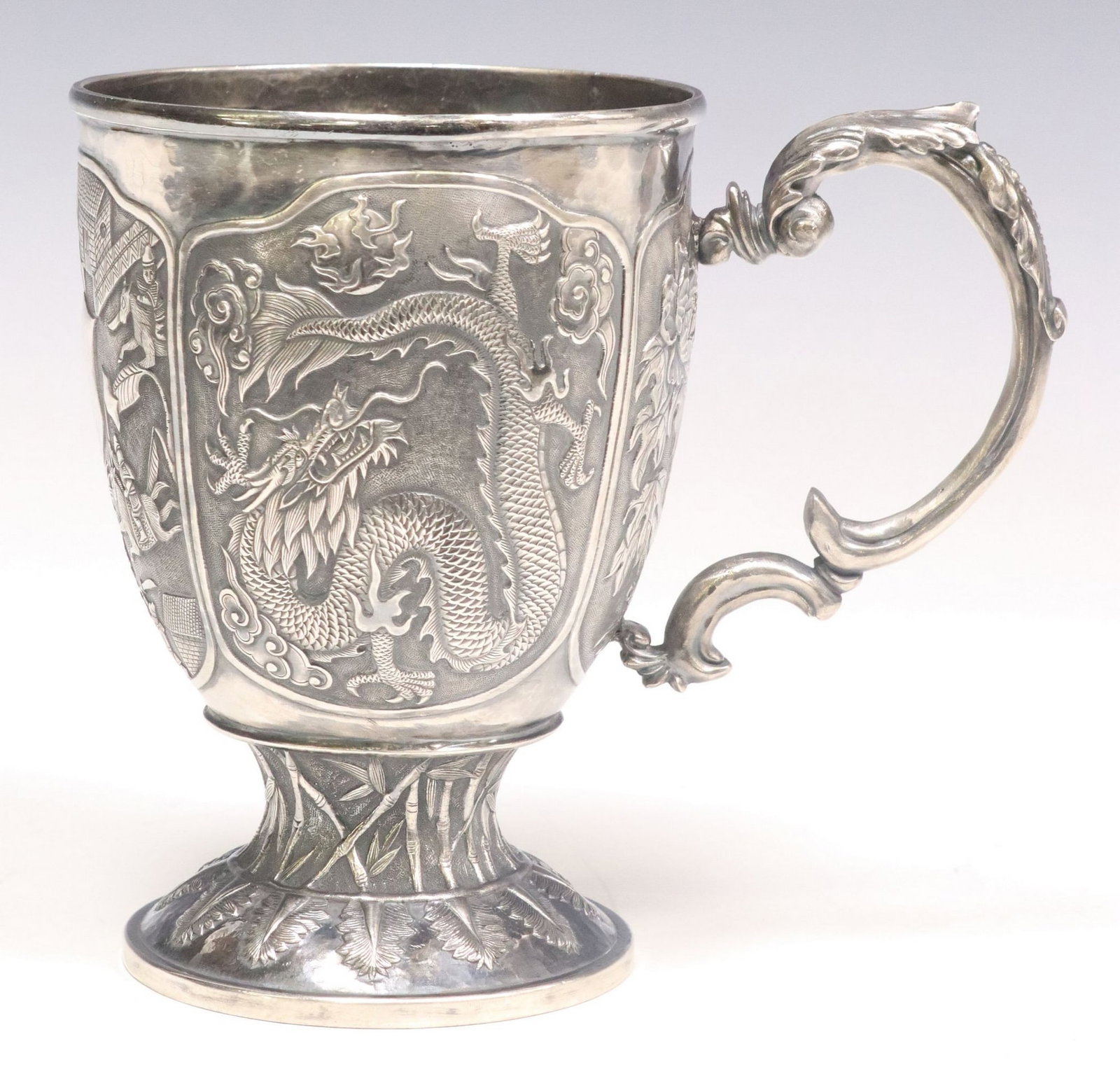 CUTSHING CHINESE EXPORT REPOUSSE SILVER MUG: Chinese Export silver mug, Cutshing (fl.1790-1895), Canton, foliated scroll handle, the body with repousse cartouches depicting warrior combat scene with central shield, mountainous landscape, florals