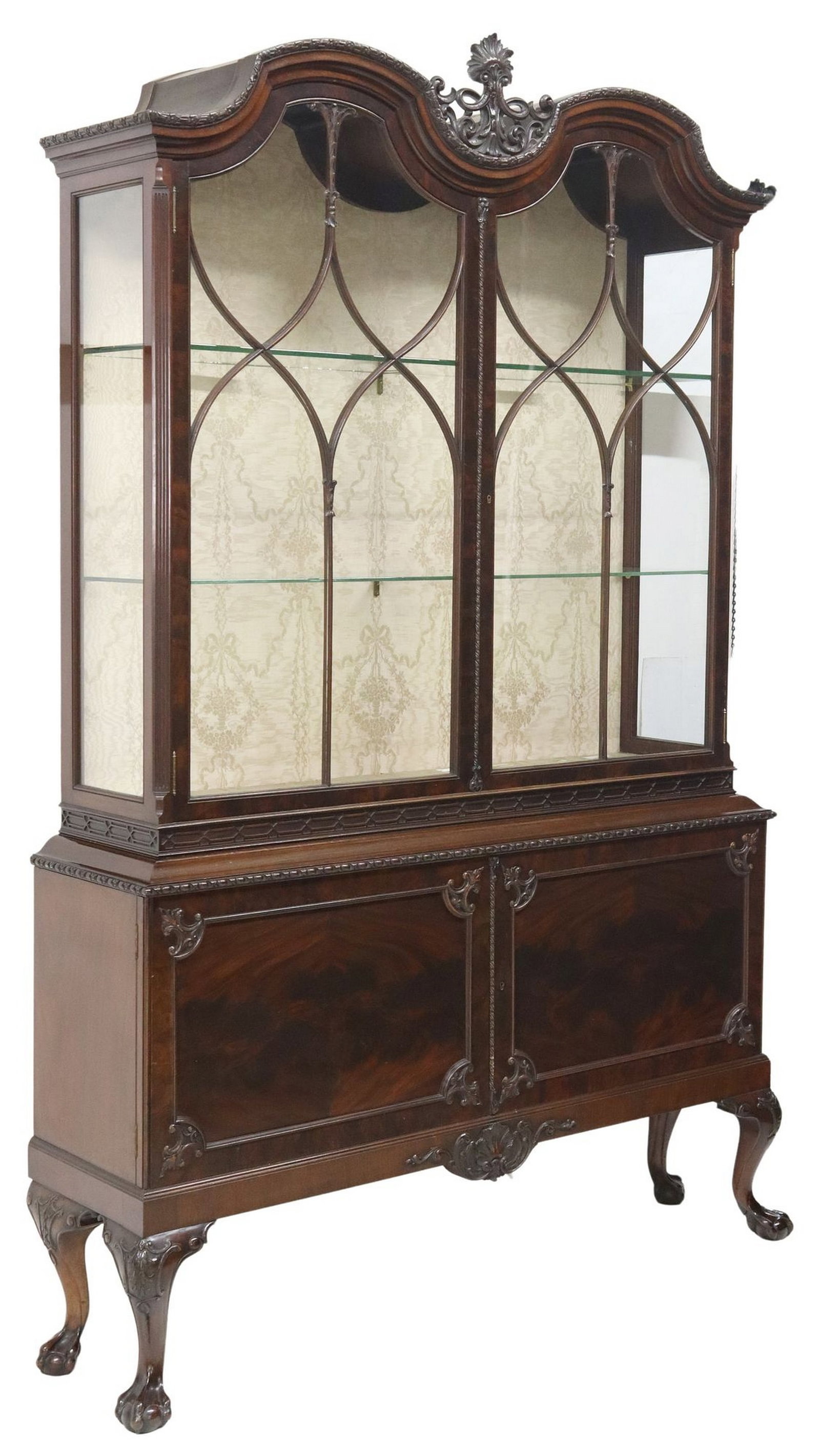 ENGLISH CHIPPENDALE STYLE CARVED MAHOGANY DISPLAY CABINET: English Chippendale style mahogany vitrine/ display cabinet, early 20th c., double arched pediment, glazed and mullioned doors, lined interior with two glass shelves, lower case with two cabinet doors