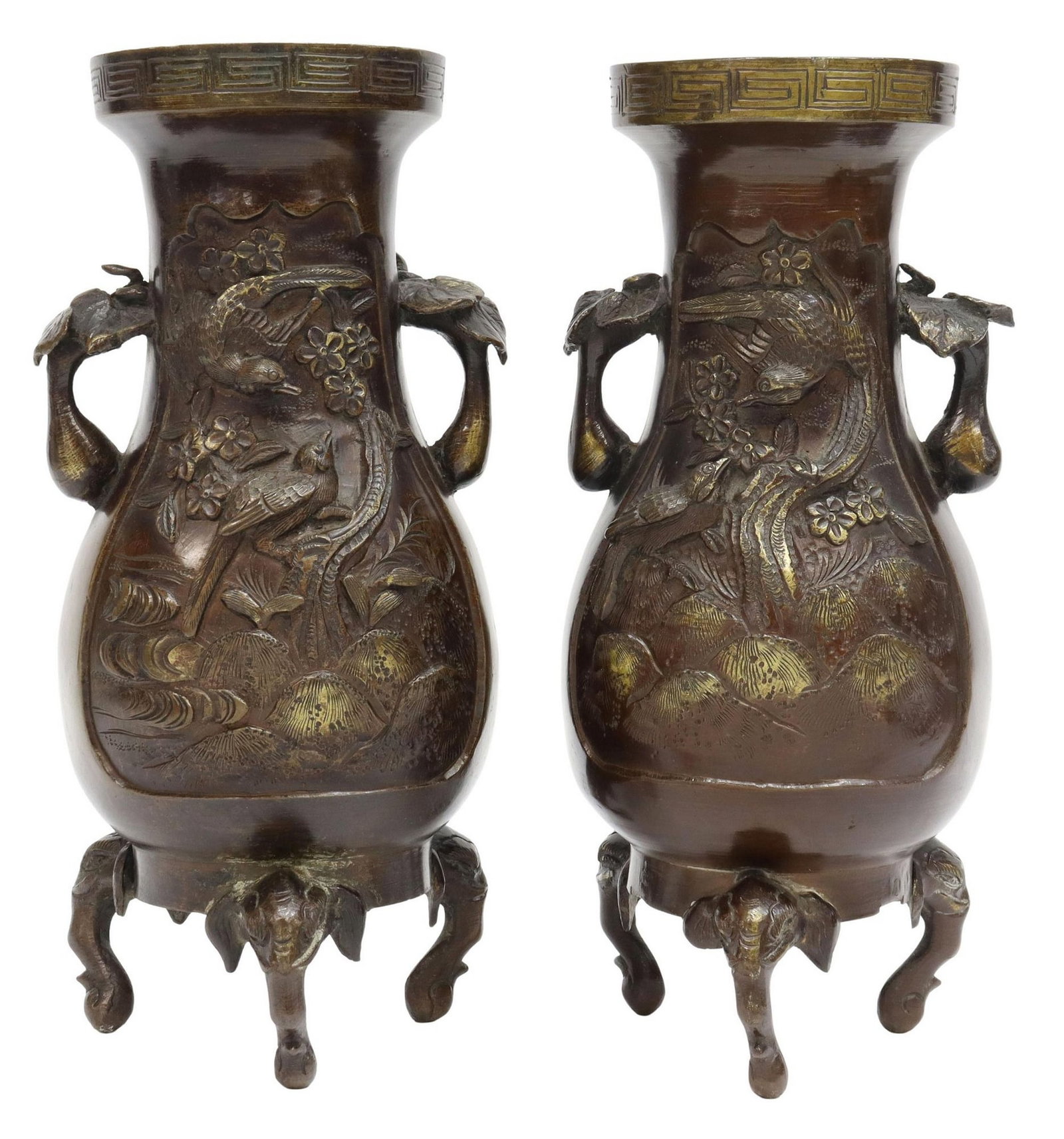 (2) JAPANESE PATINATED BRONZE VASES: (pair) Japanese patinated bronze vases/ urns, rim with meander pattern, foliate handles, bodies with birds and insects in relief, rising on three feet modeled as elephant heads, lacking base pane