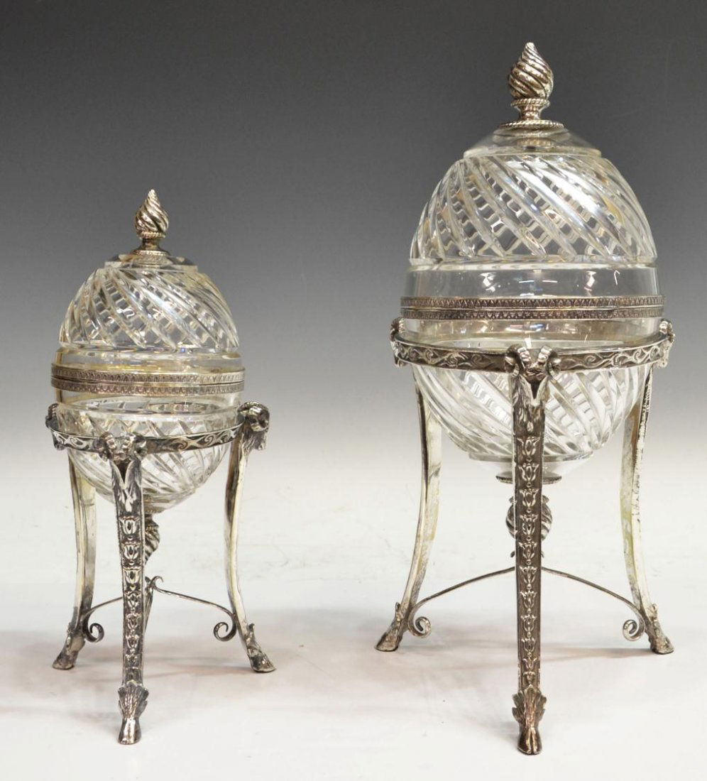NEOCLASSICAL STYLE SILVER PLATE CUT GLASS CASKETS: (lot of 2) Neoclassical style egg-form cut glass caskets fitted in silver plated stands, varied size, the colorless bowl and cover of each in feather pattern, each held by a plated stand featuring ram