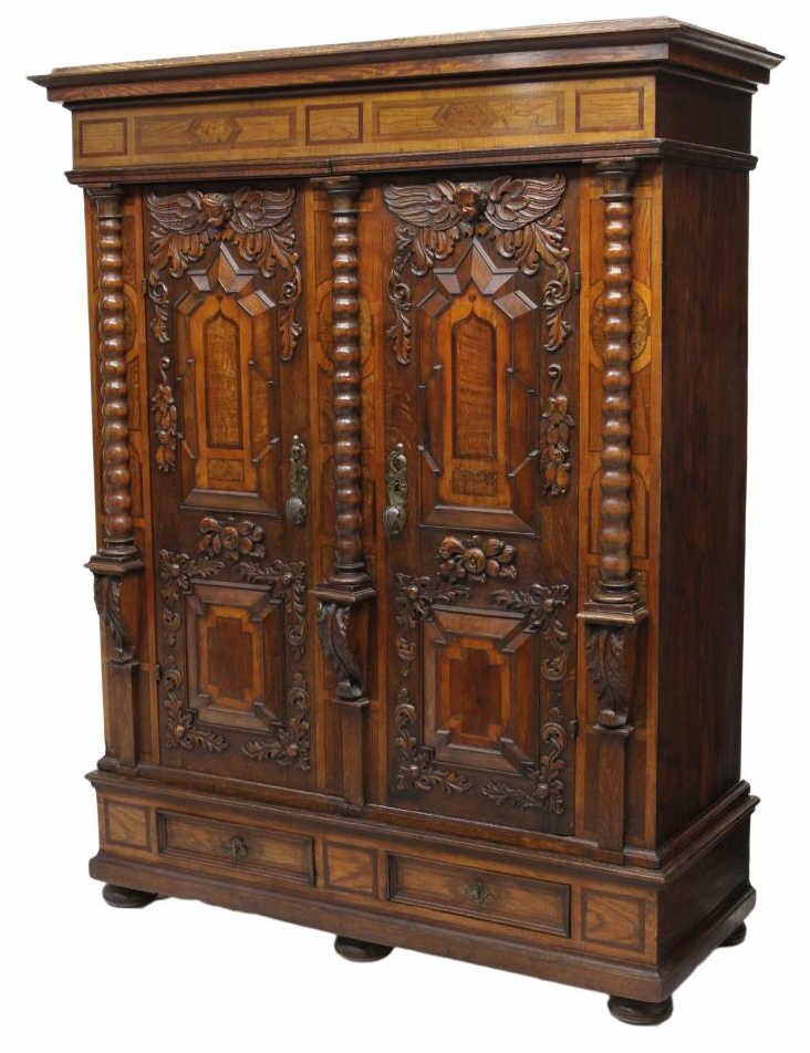 GRAND CONTINENTAL FIGURAL CARVED BAROQUE CABINET: Grand Baroque figural carved oak cabinet, 18th c., a stepped overhang cornice above the inlaid frieze, two substantial relief carved doors featuring winged cherub masks, fruit and foliate pendants and