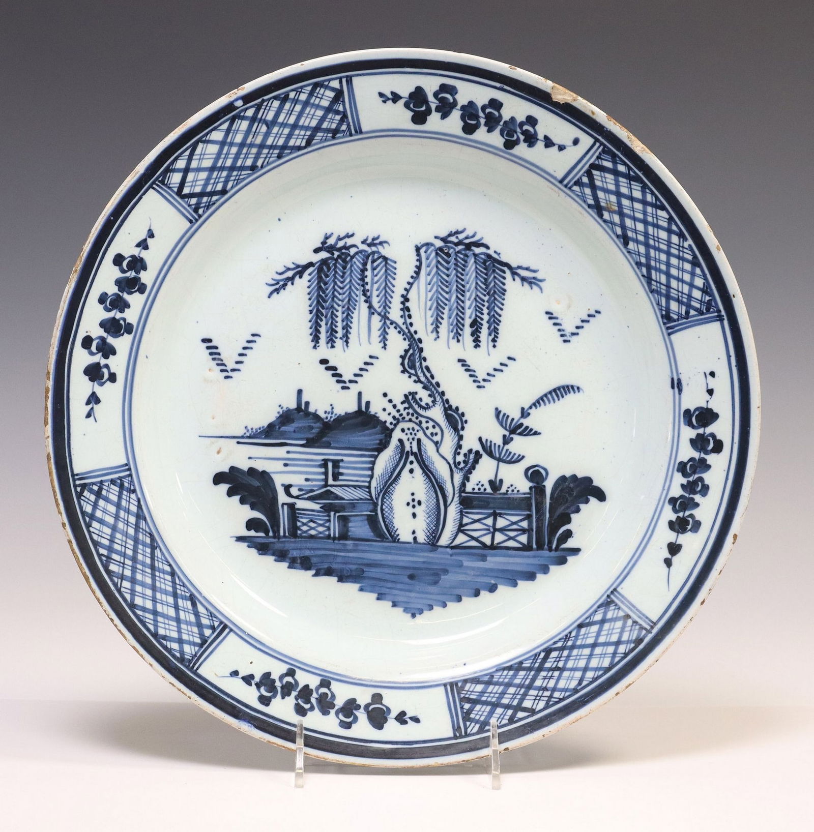 DELFT BLUE & WHITE CHINOISERIE WATERSIDE LANDSCAPE CHARGER: Delft tin-glazed earthenware charger, late 18th c., alternating floral sprigs and diaper pattern, enclose a Chinoiserie landscape with trees and flowers, typical small chips and glaze losses