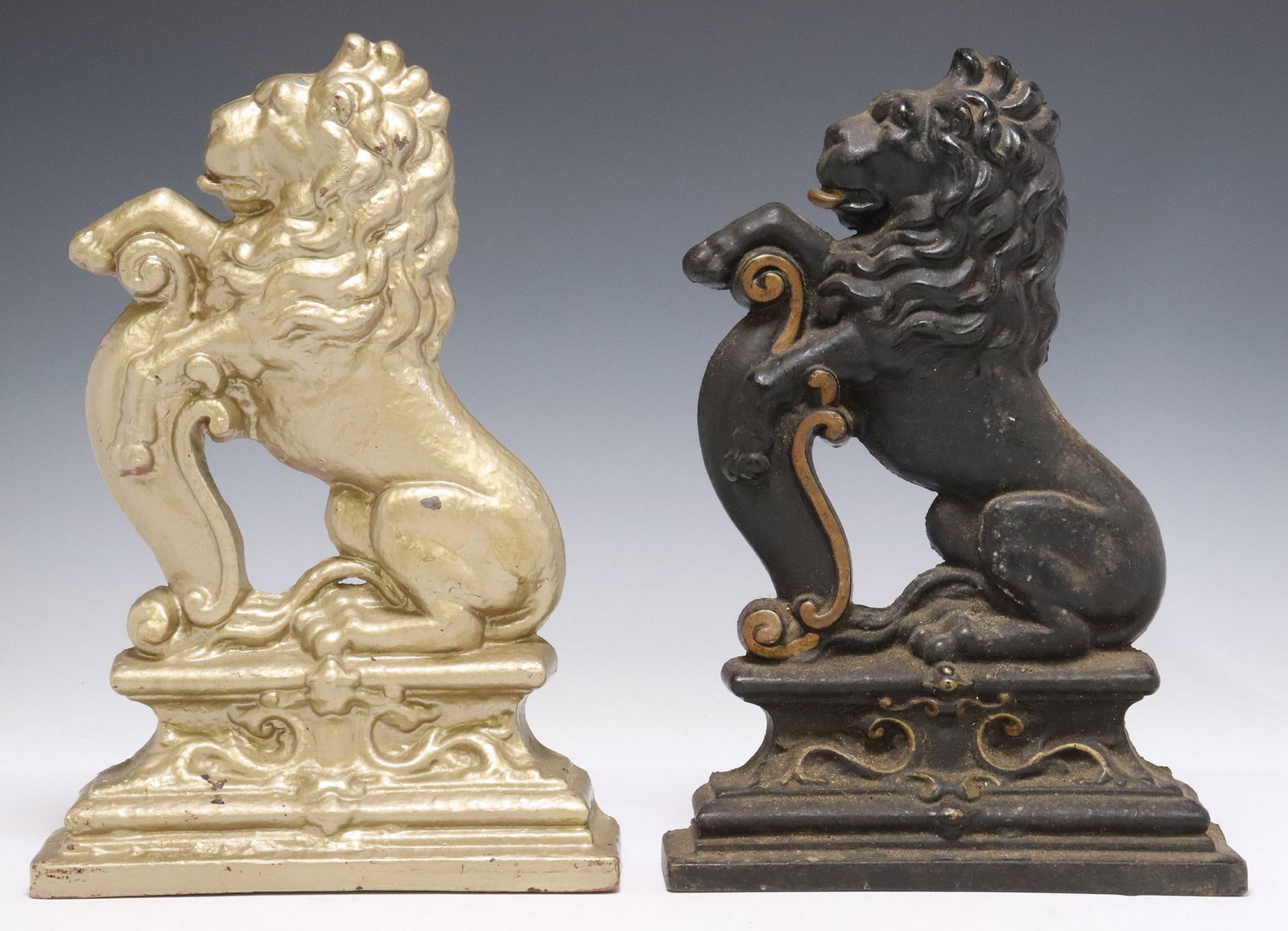 (2) PAINTED CAST IRON LION SEJANT-RAMPANT DOOR PORTERS: (lot of 2) Painted cast iron door porters/ door stops, early 20th c., each modeled as a lion sejant-rampant, resting on a plinth base, (one) in a gilt finish, (one) in a patinated finish with gilt pai
