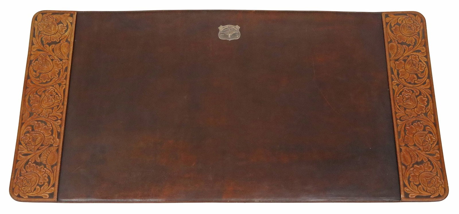 EDWARD H. BOHLIN CARVED BROWN LEATHER DESK BLOTTER: Western brown leather desk pad or blotter, Edward H. Bohlin, Hollywood, California, carved leather side panels with floral and foliate motif, silver shield-form mount marked "Edward H. Bohlin/ Sa