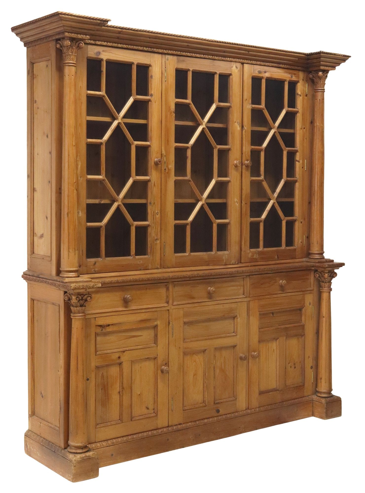 LARGE VICTORIAN STYLE PINE THREE-DOOR BOOKCASE: Large Victorian style carved pine bookcase, 20th c., step molded cornice, three glazed cabinet doors flanked by fluted columns, lower case fitted with three drawers, over three paneled cabinet doors, 