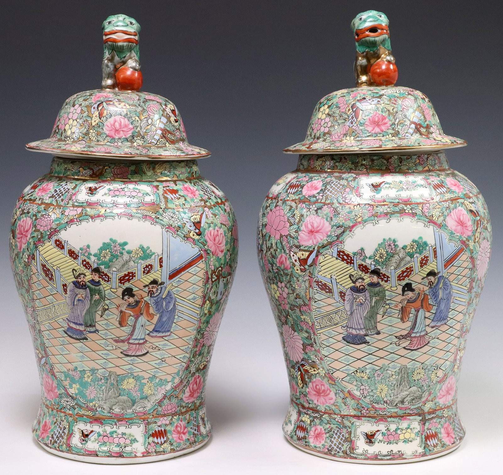 (2) CHINESE CANTON FAMILLE ROSE PORCELAIN TEMPLE JARS: (pair) Chinese famille rose enameled porcelain lidded temple jars, each having figural finial modeled as a foo dog with paw on ball, figural courtyard scenes, among rose medallions, butterflies, and f
