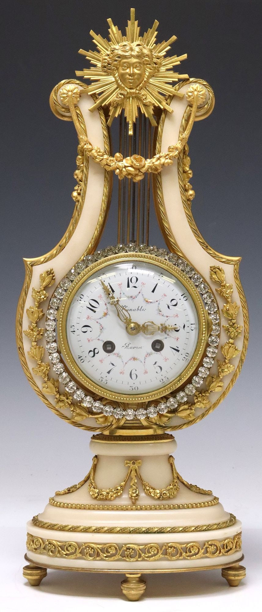 FRENCH LOUIS XVI STYLE ORMOLU & WHITE MARBLE 'JEWELED' LYRE CLOCK: French Louis XVI style lyre-form mantel clock, late 19th c., white marble case with bronze dore mounts, sunburst mask of Apollo above a draped floral swag, wreath of colorless paste stones framing the