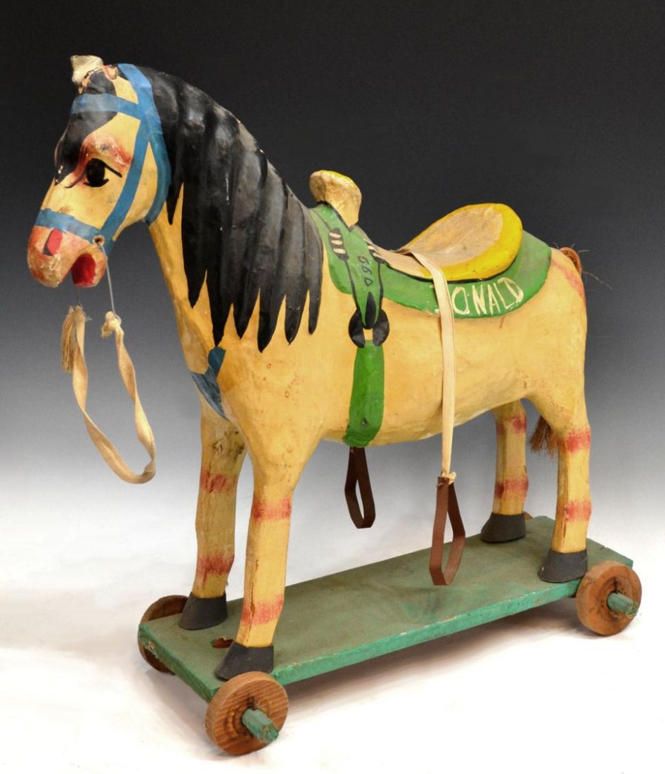 FOLK ART PAPER-MACHE HORSE ON WHEELS, MEXICO: Mexican folk art papier-mache horse, yellow and green saddle personalized with 'Donald', accompanied by dangling metal stirrups, straw tail, on green wheeled base, lacking one ear, some wear consisten