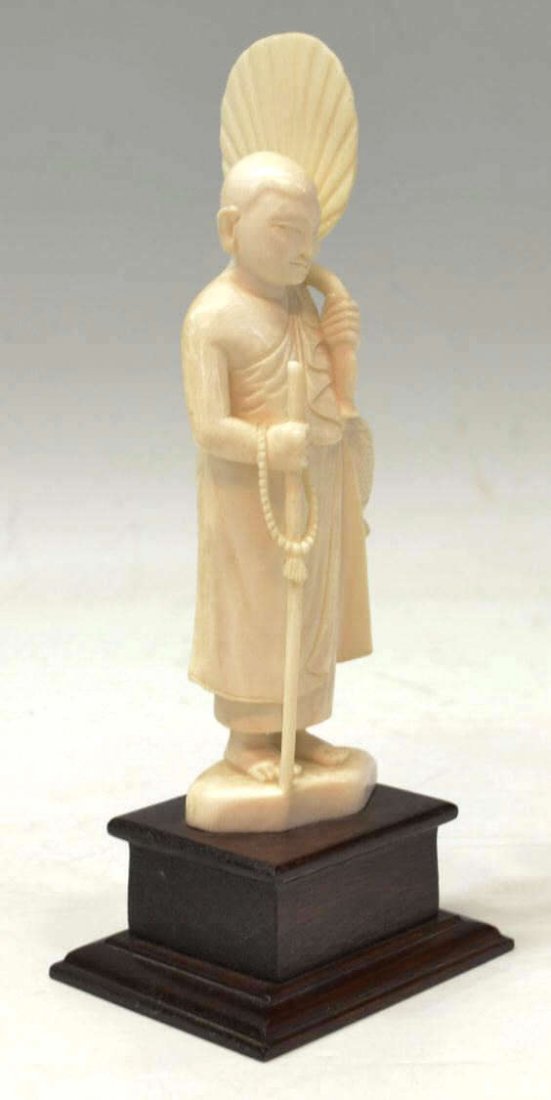 SOUTHEAST ASIAN FIGURAL IVORY CARVING OF A MONK: **International shipping is not available on this lot** Southeast Asian figural ivory carving, Thailand, a revered monk clad in simple drapery, standing with a fan and basket suspended from his left a