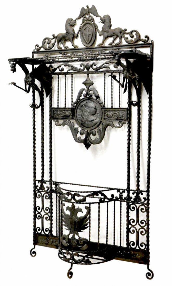 SPANISH IRON HALL TREE, LARGE WINGED GRIFFINS: Spanish black wrought iron hall tree in the manner of Antonio Gaudi (Antoni Gaudí, Cornet, Spain, 1852-1926), last quarter 19th c., a pair of large winged griffins support the upper crest with coat o