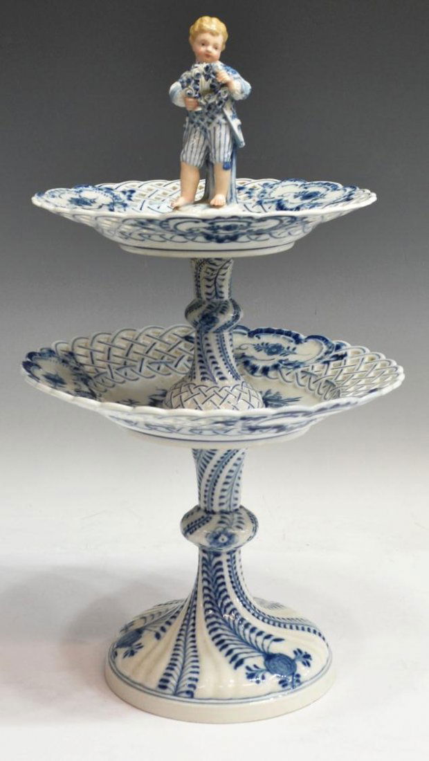 MEISSEN FIGURAL BLUE ONION TWO TIER SERVER: Meissen Blue Onion porcelain server, 20th c., surmounted by child figure holding wreath, two graduated reticulated tiers, set on conforming oval base, three visible cross sword marks, damage as pictur