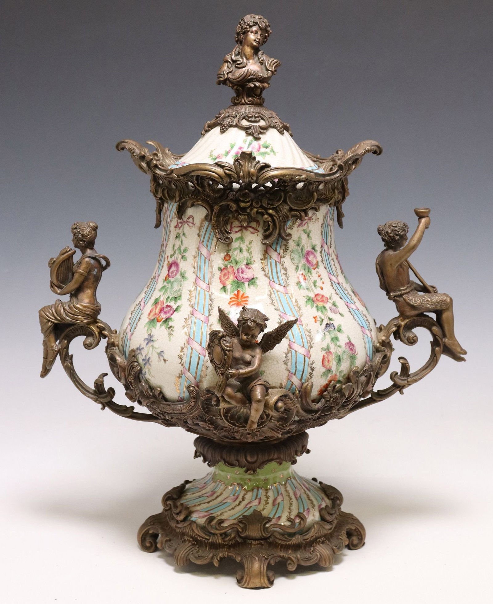 NEOCLASSICAL STYLE BRONZE-MOUNTED PORCELAIN CENTERPIECE URN: Neoclassical style parcel gilt porcelain centerpiece urn, Wong Lee, late 20th c., having figural finial modeled as a female bust, over reticulated foliate trim, bulbous body with polychrome floral mot