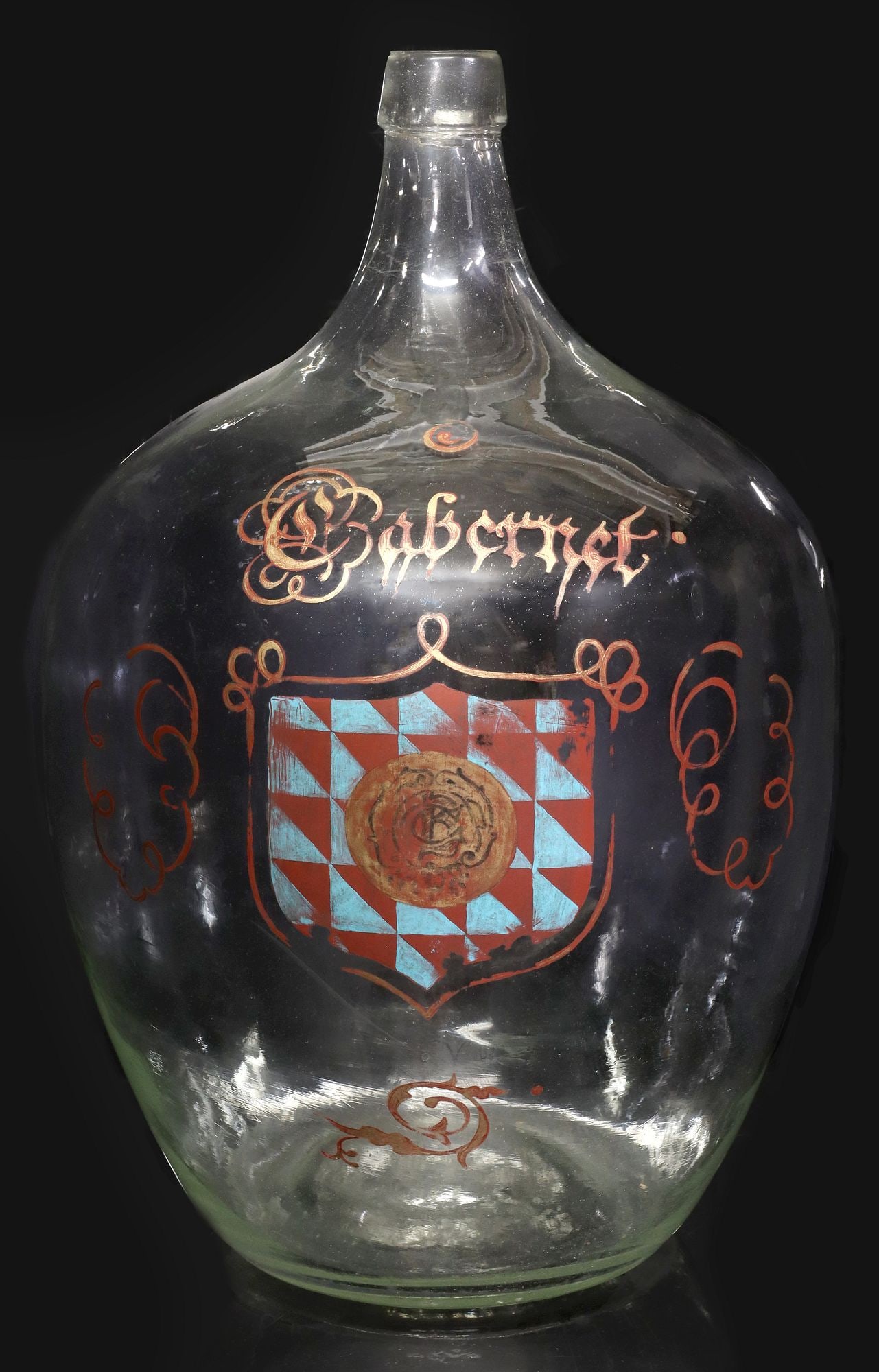 FRENCH BLOWN GLASS CABERNET CARBOY / DEMIJOHN WITH COAT OF ARMS: French colorless blown glass carboy or demijohn bottle, having slim tapered neck, over bulbous body, with polychrome painted inscription "Cabernet," above checkered coat of arms wi