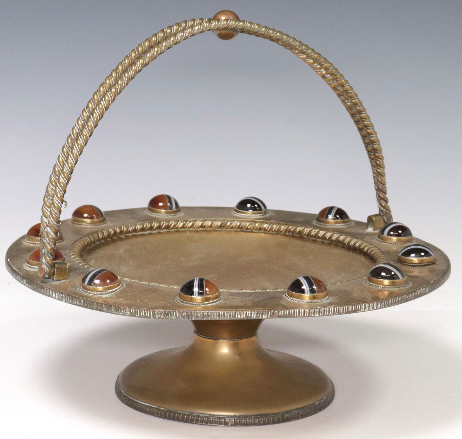 BRITISH ARTS & CRAFTS BRASS TAZZA OR BASKET: British Arts and Crafts brass tazza/ basket, early 20th c., rim with Celtic-style design of interlacing knots, banded agate cabochons, on a pedestal base, approx 6.75"h, 12"diam, 4.5lbs