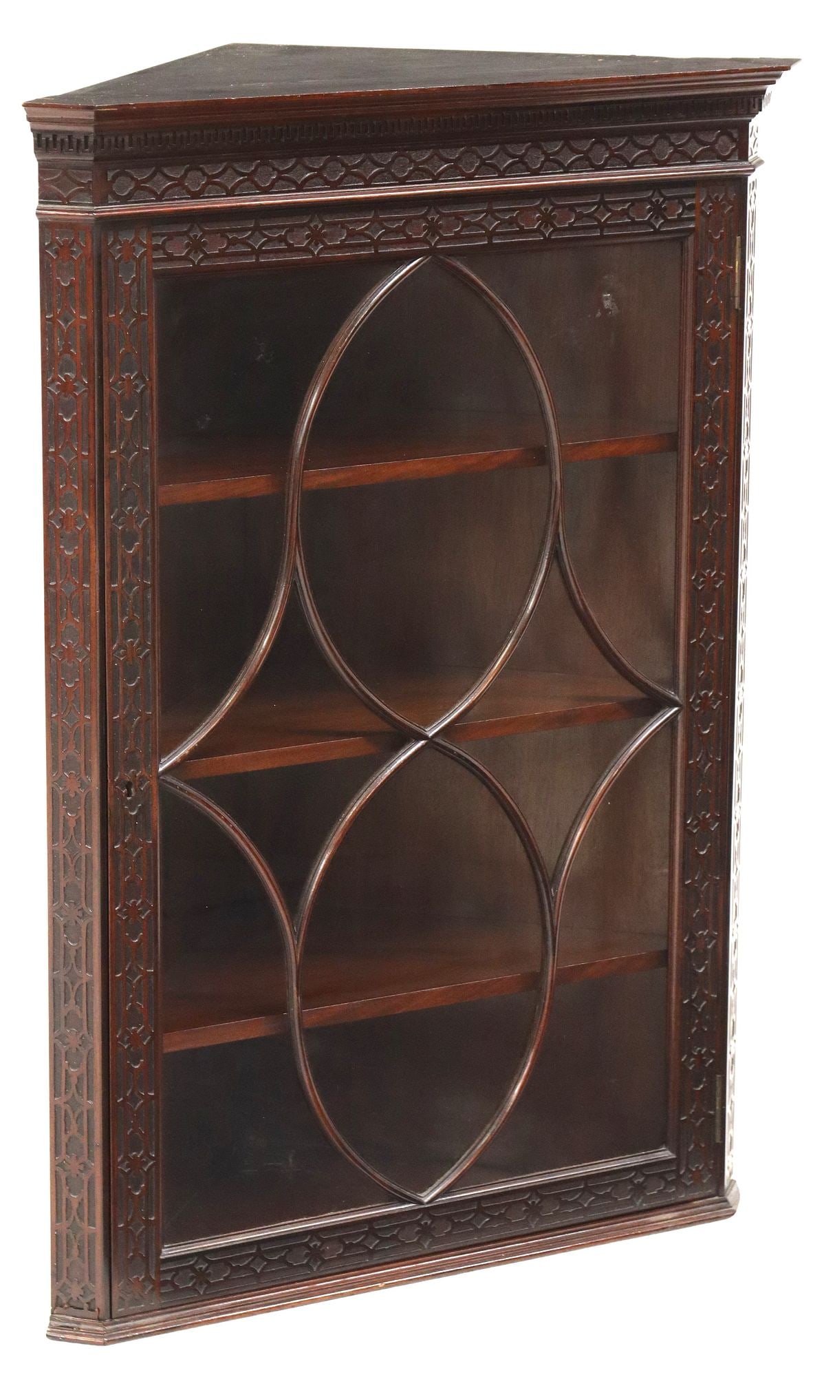 GEORGIAN STYLE CARVED MAHOGANY CORNER CUPBOARD: English Georgian style mahogany corner cupboard, early 20th c., molded cornice, above a single cabinet door with geometric astragals, the angled corners carved with blind fretwork, interior shelves, a