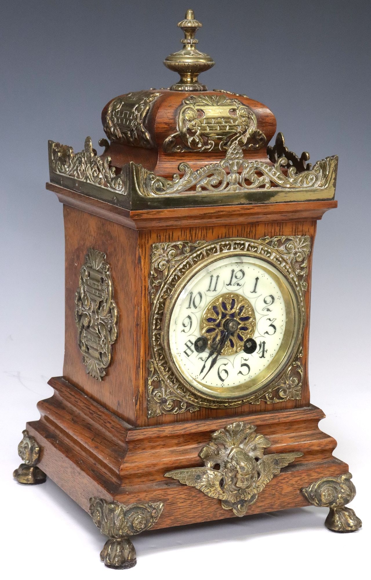 ENGLISH VICTORIAN BRASS-MOUNTED OAK BRACKET CLOCK: English Victorian brass-mounted oak mantle clock, late 19th c., having turned-form finial, over scrolled foliate gallery, stepped rectangular case with central glazed dial viewing door, enameled 