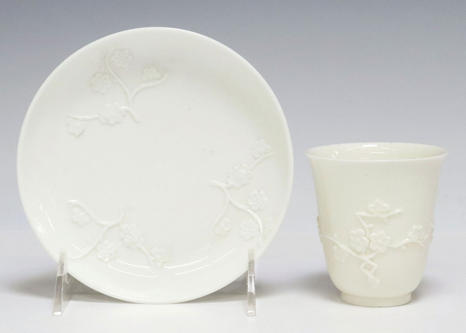 EARLY CAPODIMONTE 'BLANC DE CHINE' PORCELAIN BEAKER & SAUCER: Early Italian "blanc de Chine" porcelain beaker and saucer, Capodimonte, 18th c., after examples from the Dehua kilns in China, molded decoration of flowering prunus branches in relief, beaker with a