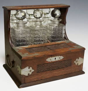 ENGLISH VICTORIAN OAK TANTALUS & GAMES COMPENDIUM: English Victorian oak tantalus/ games compendium, late 19th,&nbsp;with carved floral medallions and patinated metal&nbsp;mounts, dual side handles, housing three molded glass decanters and cut stopper