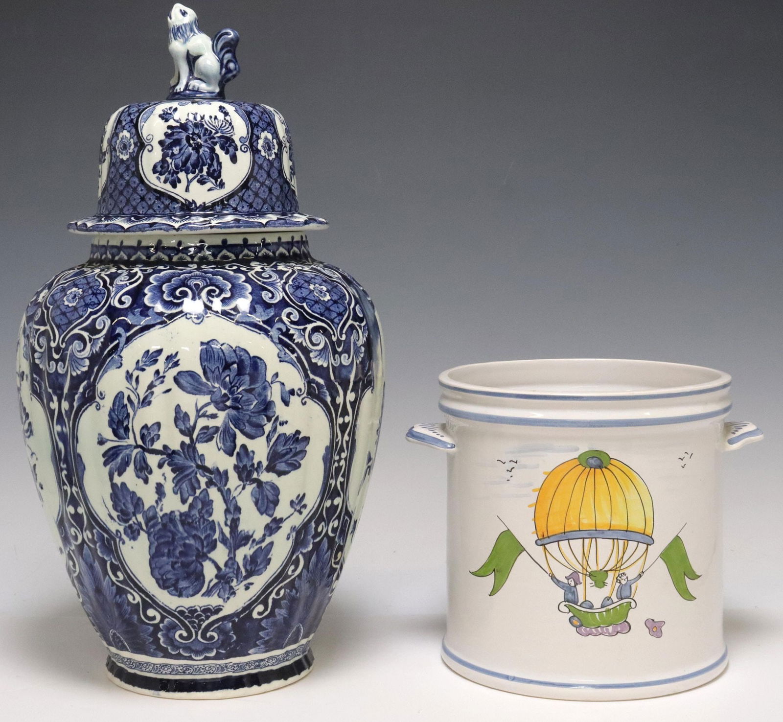 (2) PIERRE DEUX FAIENCE BOTTLE COOLER & DELFT RIBBED VASE & COVER: (lot of 2) Tin-glazed earthenware, including: (1) Delft blue and white vase and cover, domed cover surmounted by a lion-form finial, ribbed baluster body decorated with floral spray and foliates,