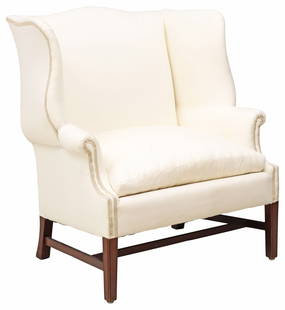 LARGE CHIPPENDALE STYLE BEIGE-UPHOLSTERED WINGBACK ARMCHAIR: Oversized Chippendale style upholstered wingback armchair, 20th c., having scalloped back and scrolled arms, removable seat cushion, in beige fabric upholstery, with ribbon trim, rising on stretcher-j
