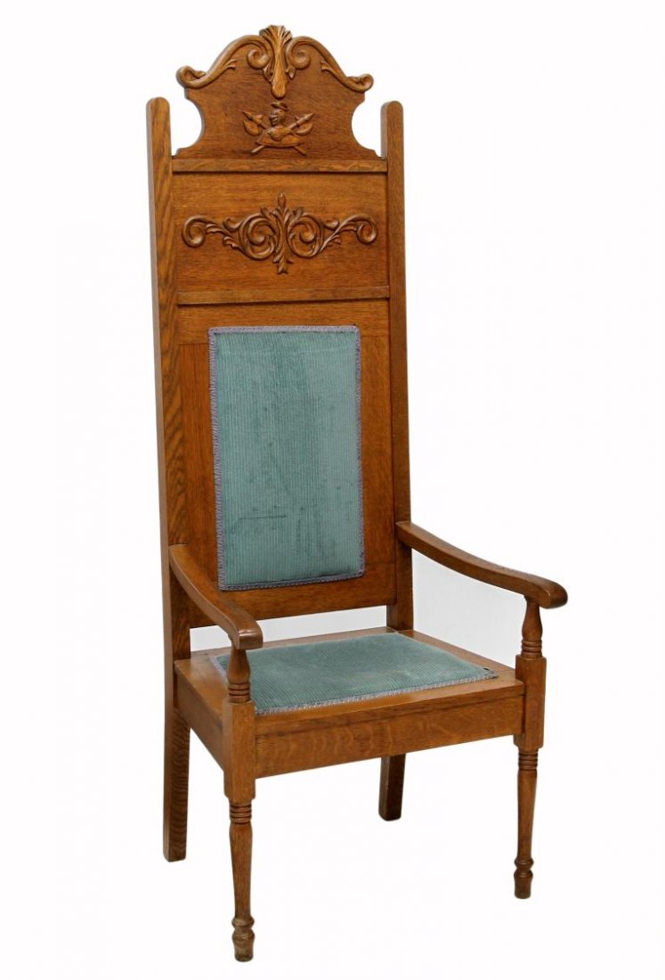 GERMAN OAK HIGHBACK ARM CHAIR: German highback oak chair having a shaped crest with applied carving including a knights helmet and battle axes, two shaped arms flanking a partially upholstered back and seat, raised on turned front