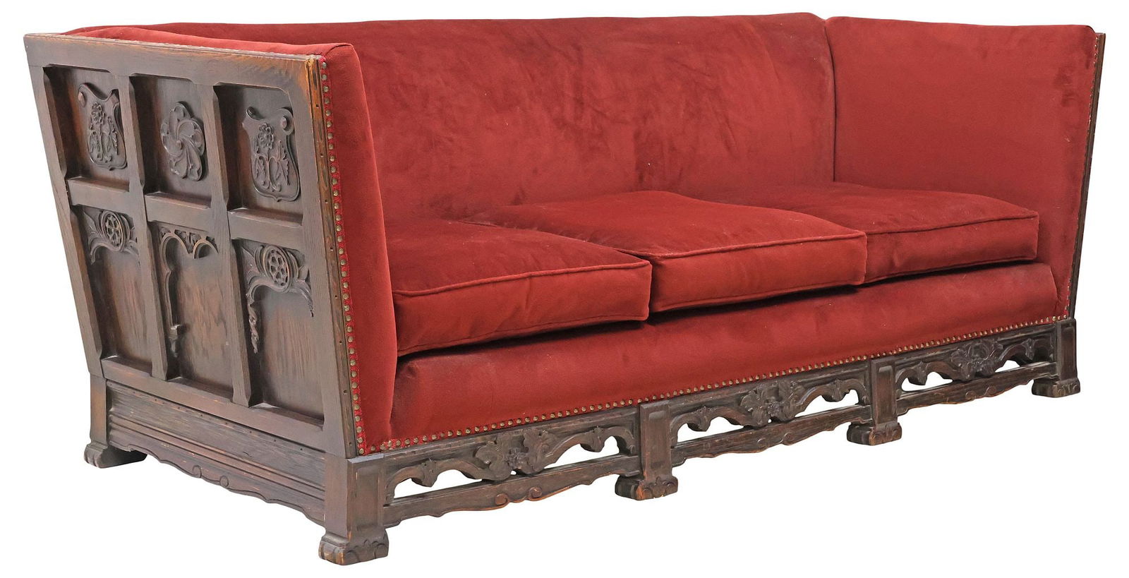 AMERICAN GOTHIC STYLE CARVED OAK VELVET-UPHOLSTERED SOFA: American Gothic style carved oak sofa, early 20th c., having padded back and seat in burgundy velvet upholstery, three removable seat cushions, back and sides with chamfered paneling, adorned with flo