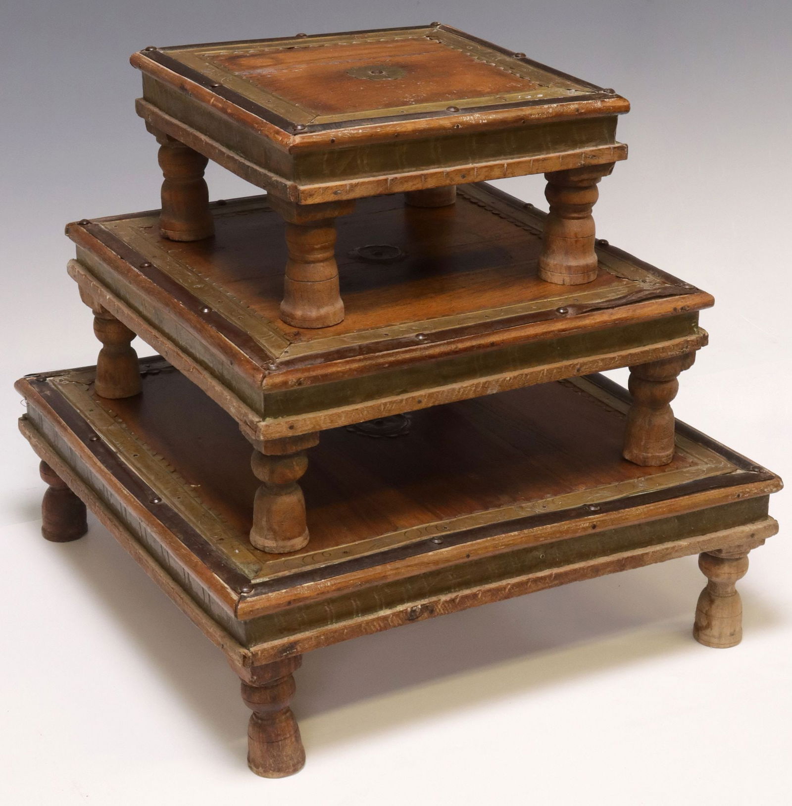 (3) SMALL METAL-CLAD TEAK BAJOT / LOW NESTING TABLES, INDIA: (lot of 3) Small metal-clad teak bajot/ low nesting tables, India, each of square form, with patinated metal trim and corner pieces, rising on turned legs, largest: approx 4.75"h, 14.4"w, 14.5"d, smal