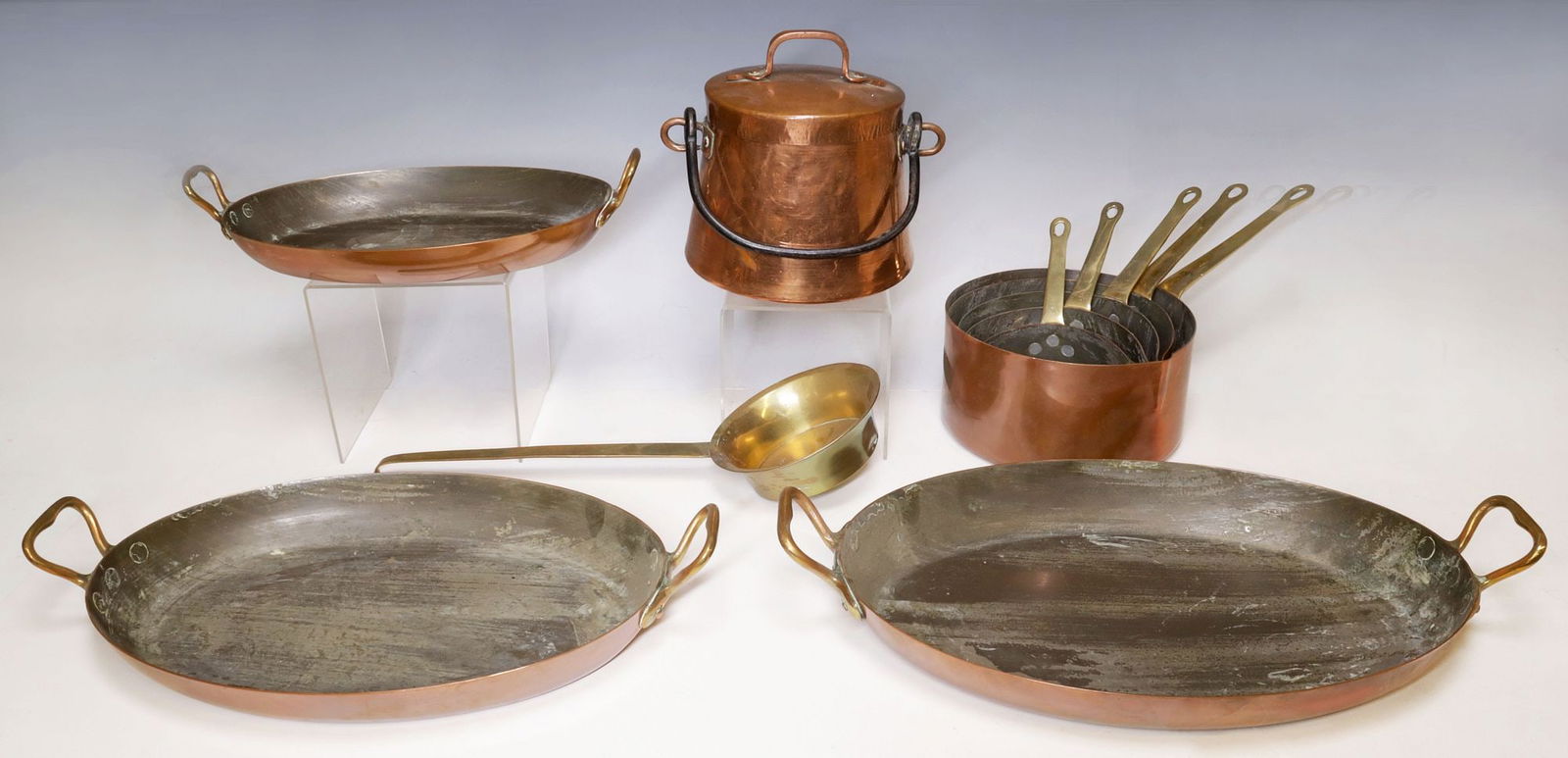 (10) COPPER & BRASS GRADUATED PANS, LADLE, & COVERED CAULDRON: (lot of 10) Copper and brass kitchenware, all unmarked, including: (3) graduated copper gratin pans, dual brass handles, largest: approx 3.5"h, 18.75"w, 10 5/8"d, smallest: approx 3"h, 14"w, 8"d; (5)