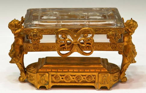 ORNATE GILT METAL & ETCHED GLASS PUTTI CASKET: French style gilt metal casket, a rectangular colorless glass divided jar with floral etched lid, fitted in an ornate gilded frame supported by a pair of robust putti caryatids, makers mark underfoot