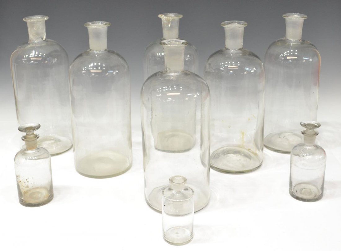 (9) ANTIQUE HAND BLOWN GLASS APOTHECARY BOTTLES: (lot of 9) Collection of antique hand blown colorless glass apothecary pharmacy bottles, two smaller retaining ground glass stoppers, some chips, two larger intact with cracks to neck, largest: 13.25"