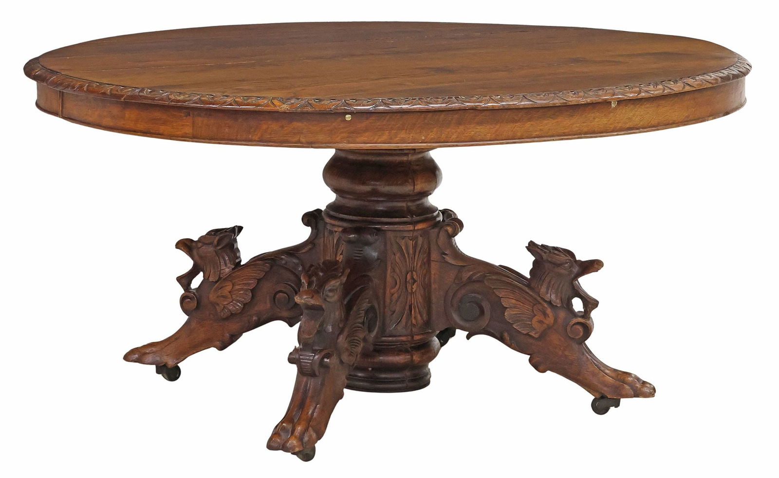 FRENCH HENRI II STYLE CARVED OAK DINING TABLE: French Henri II style carved oak dining table, late 19th c., having oval tabletop with lunette trim, rising on turned standard, carved supports modeled as winged mythical beasts with paw feet, rising