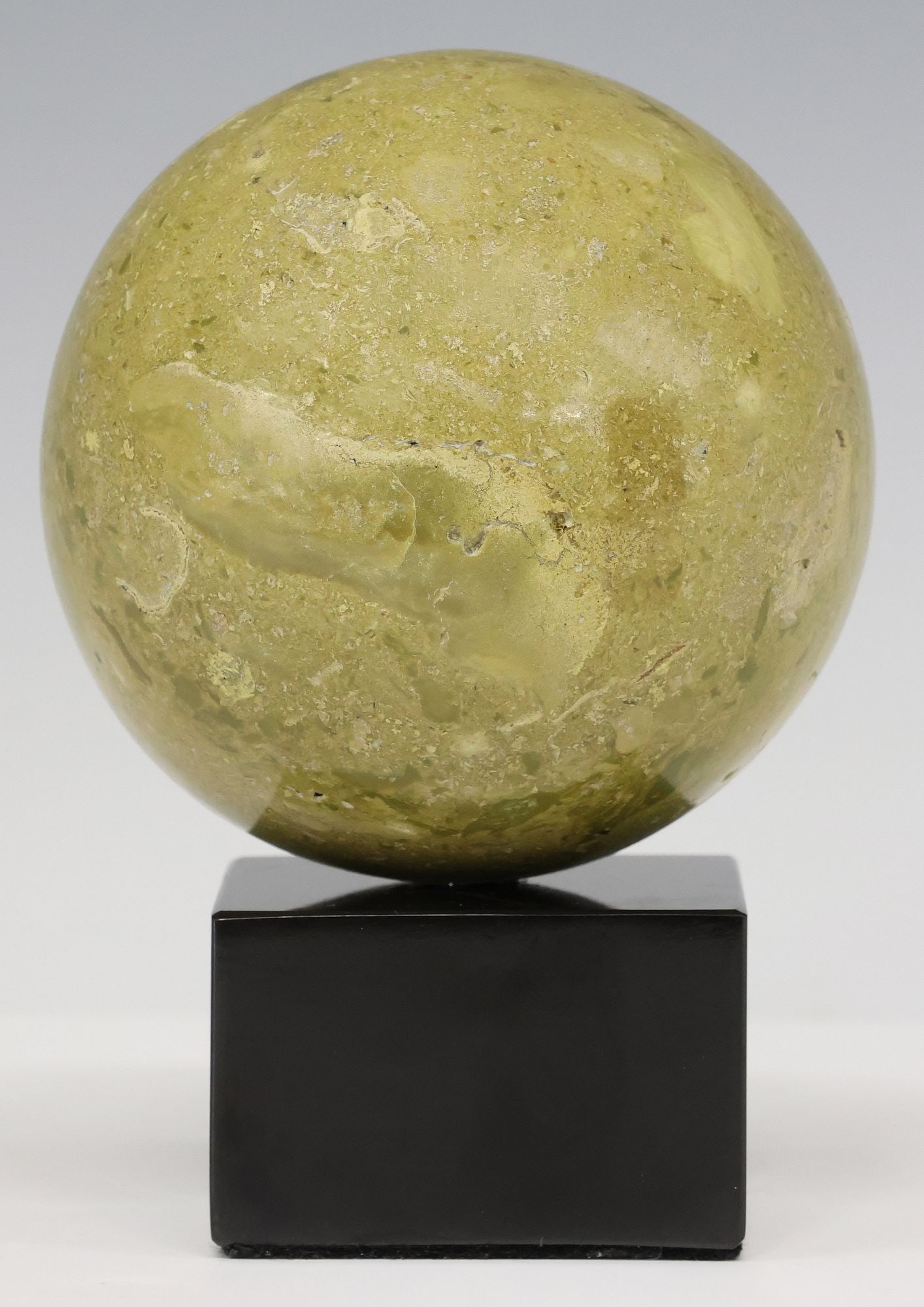 GEOLOGICAL GREEN MARBLE SPHERE ON BLACK MARBLE BASE: Geological green marble sphere, rising on black marble base, specimen: approx 4"h, 4.25"diam, overall: approx 5.75"h, 4.25"w, 4.25"d, 3.5lbs