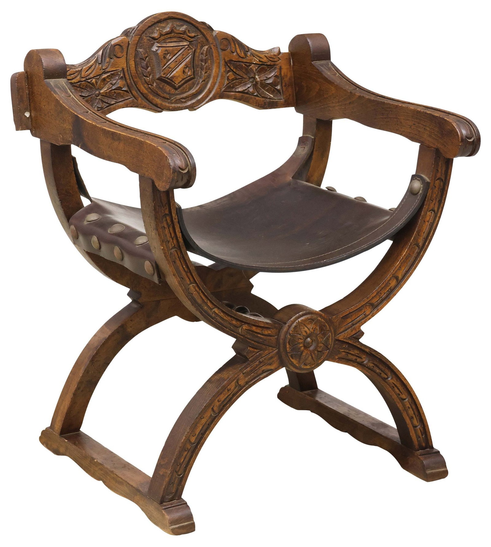 SPANISH RENAISSANCE REVIVAL CARVED WALNUT & LEATHER CURULE CHAIR: Spanish Renaissance Revival walnut curule armchair, 19th c., carved back with heraldic shield, wide armrests flanking leather sling seat, with oversized nail head trim, curule base with centered flora