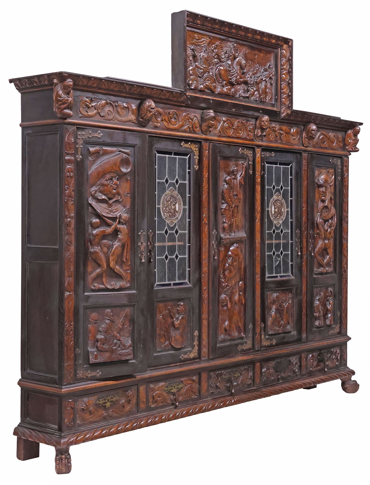 FINE SPANISH RENAISSANCE REVIVAL OAK & STAINED GLASS 'DON QUIXOTE' BOOKCASE: Spanish Renaissance Revival carved oak bookcase, 19th c., having raised pediment with figural battle scene in relief, above scrolled frieze segmented by protruding portraits and misers, fitted with fi